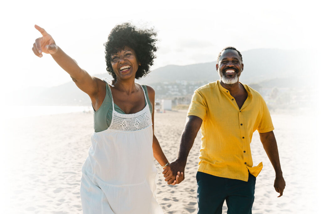 African American mature couple walking on the beach, holding hands, the woman pointing ahead towards the distance.