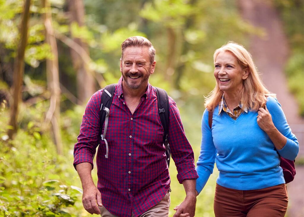 Mature Couple walking in the forest with backpacks, holding hands.