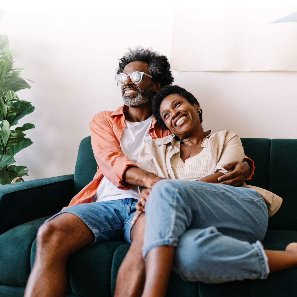 Middle-aged African-American couple embracing on a sofa, smiling.